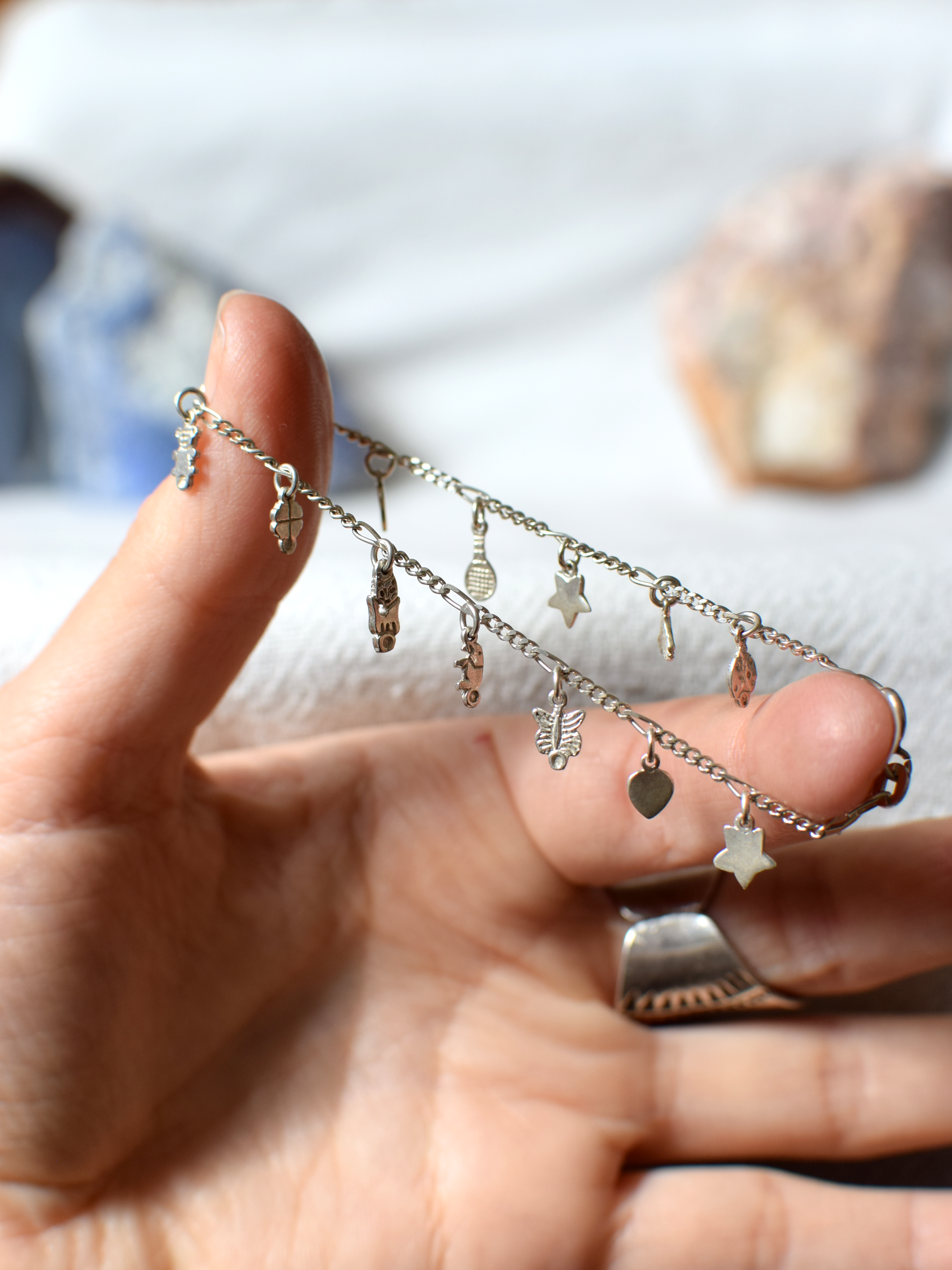 Hand holding a silver necklace with various charms against a blurred background