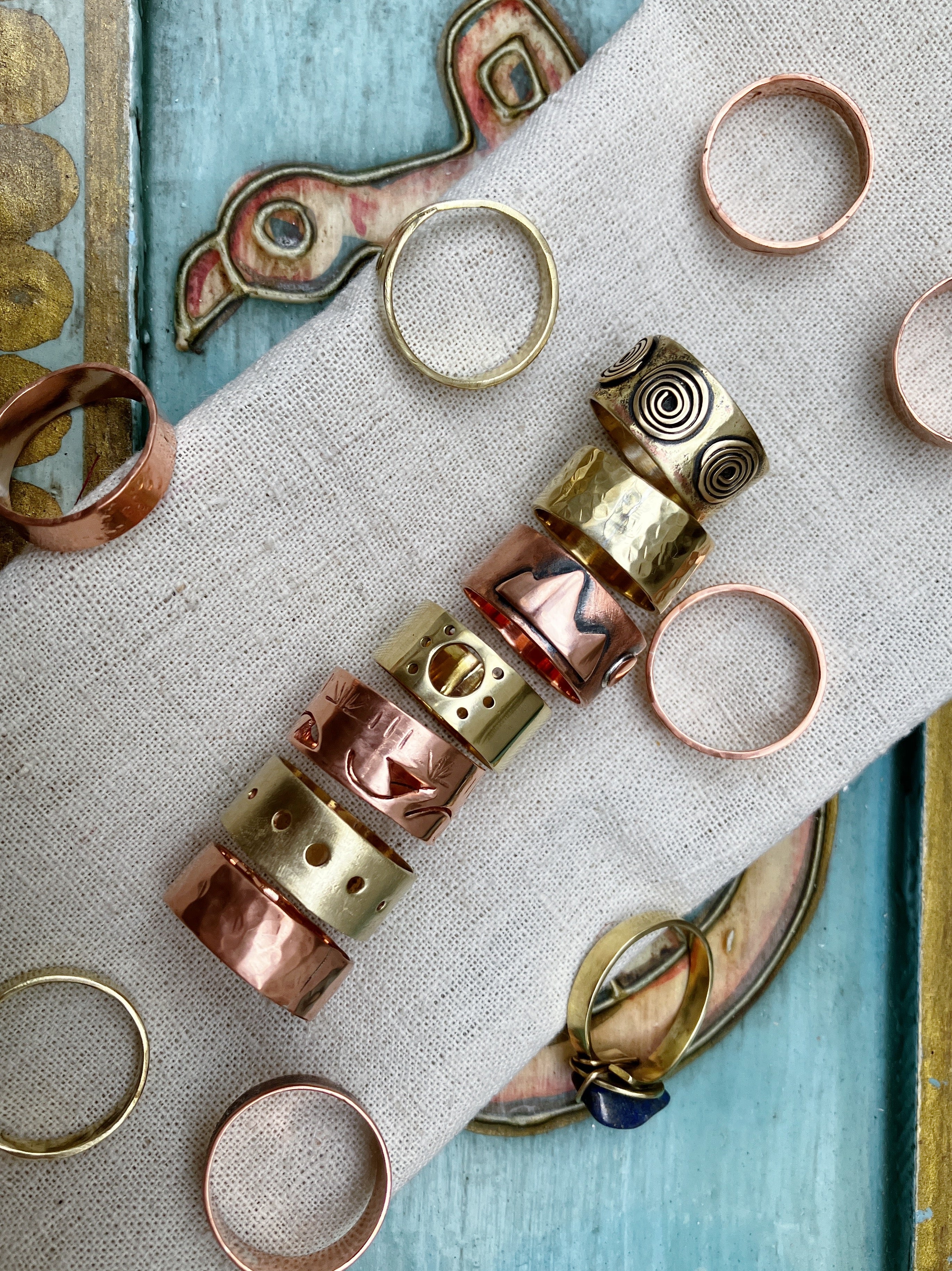 Collection of handmade copper and brass rings on a textured fabric surface