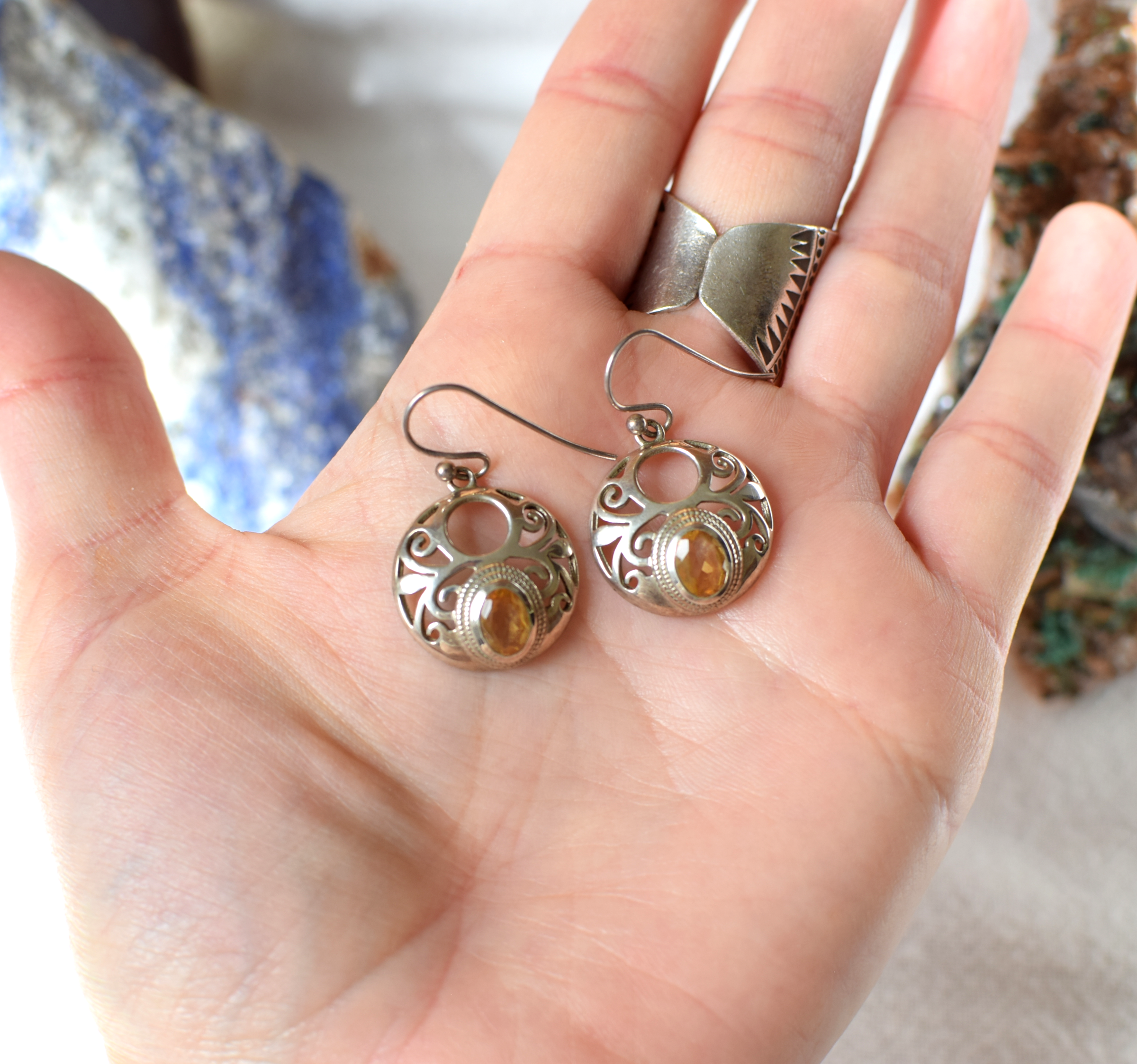 Silver earrings with gemstones held in a hand against a blurred background
