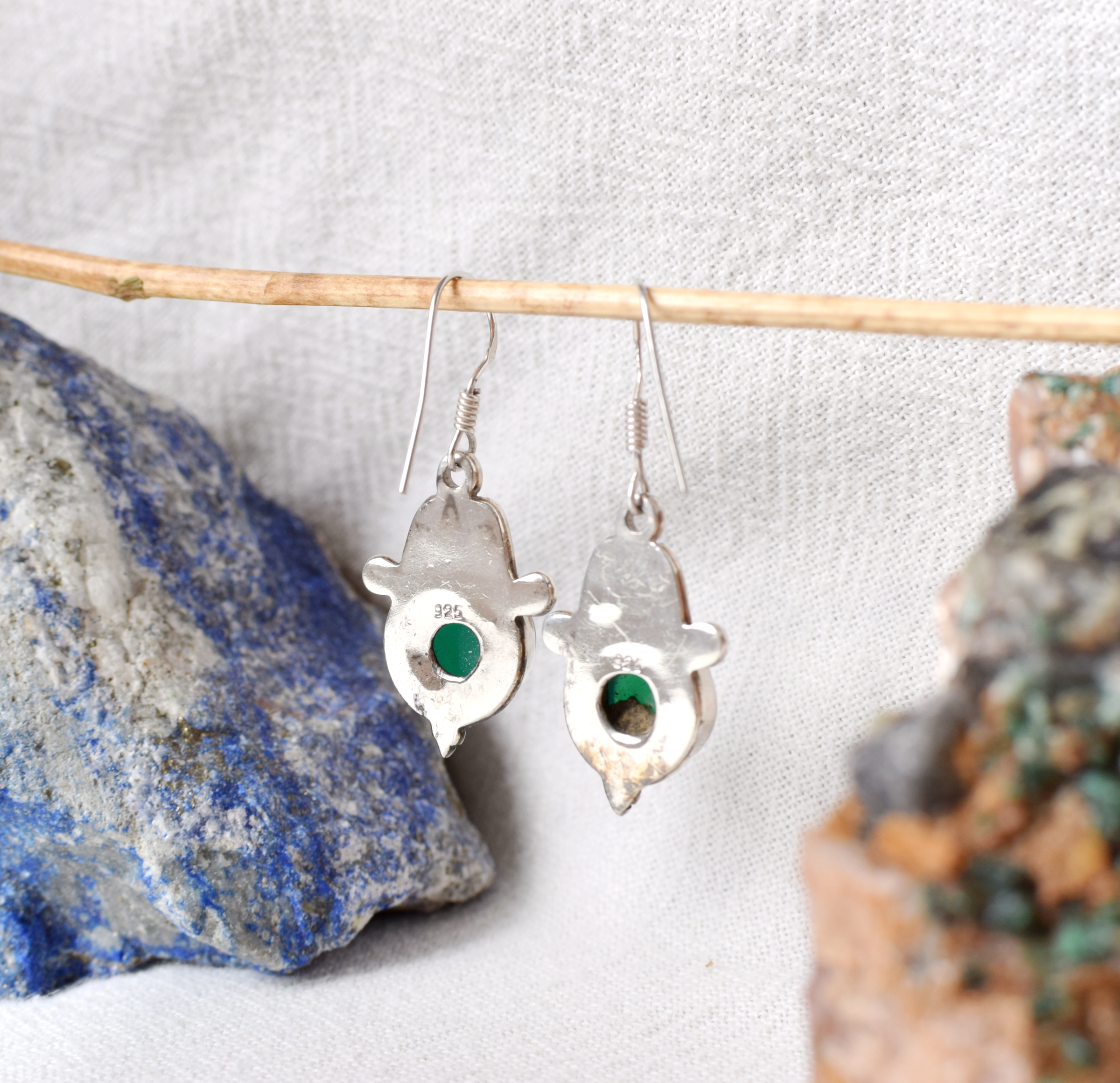 Silver earrings with green stones hanging on a branch with rocks in the background