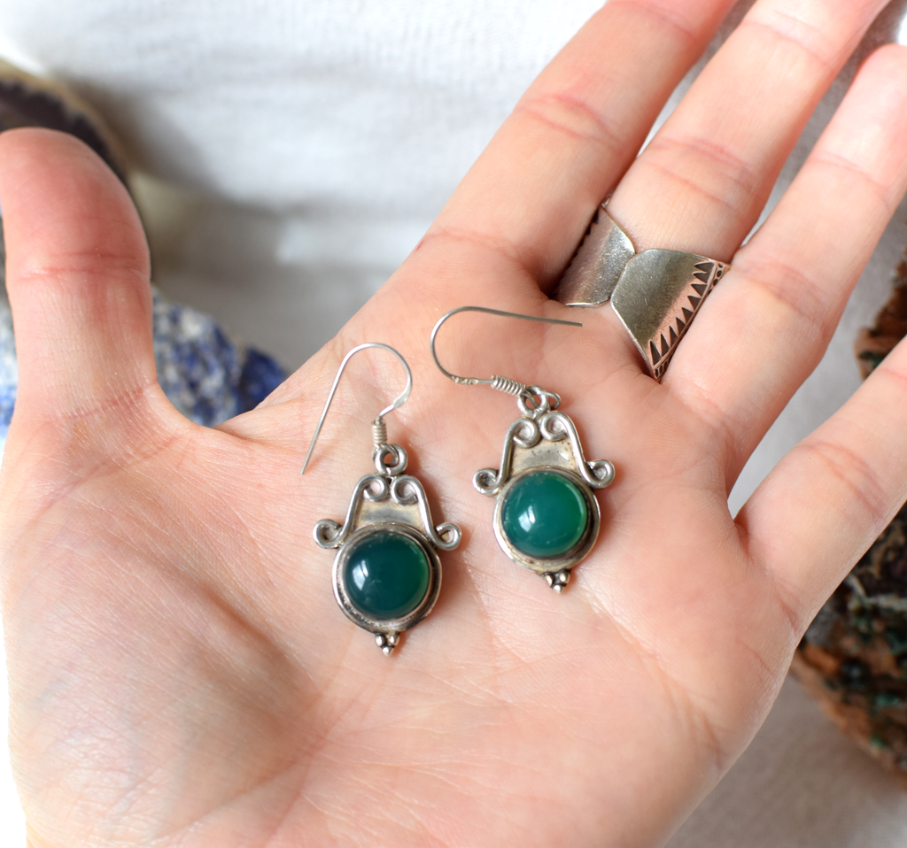 Silver earrings with green gemstones held in a hand