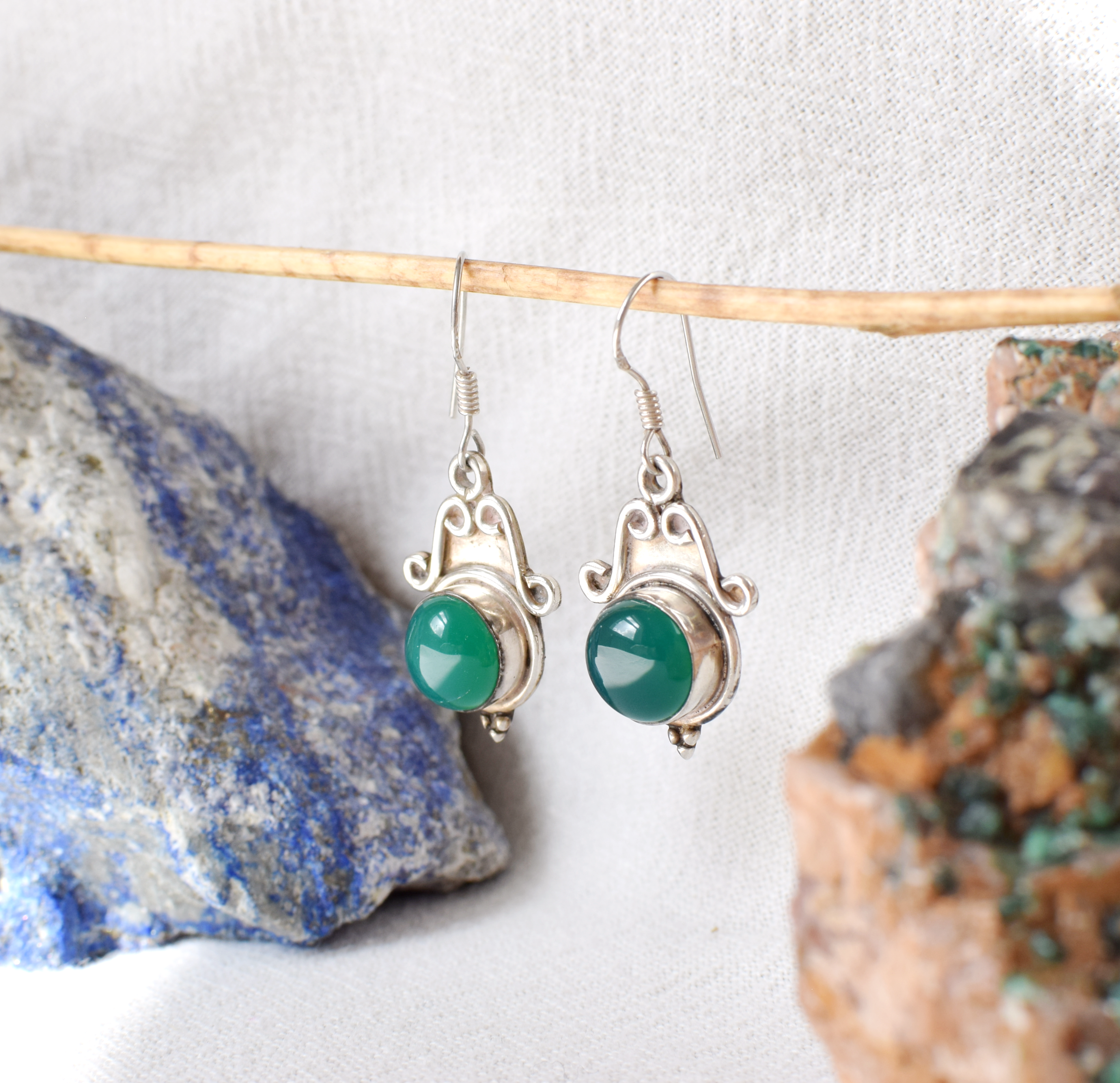 Silver earrings with green gemstones on a white background with rocks.