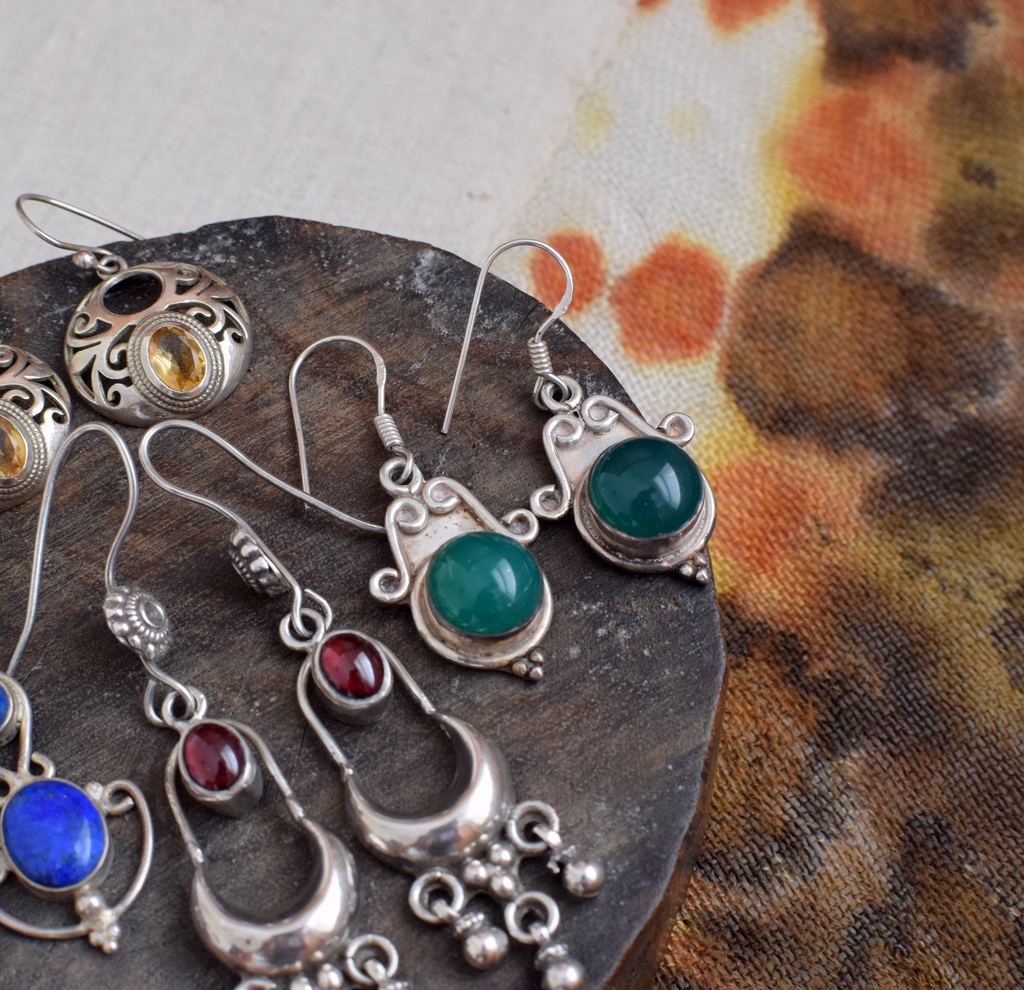 Collection of silver earrings with colorful gemstones on a textured surface