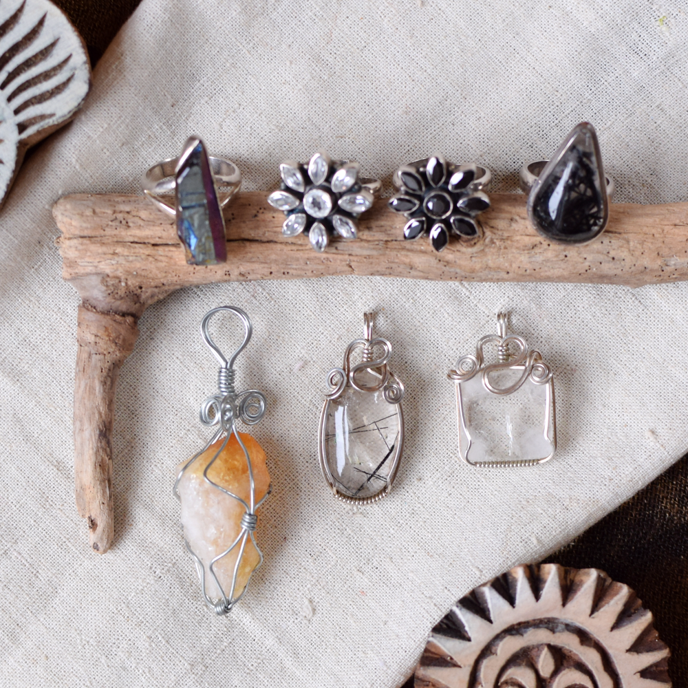 Collection of silver jewelry including rings and pendants on a natural wooden stick and fabric background.