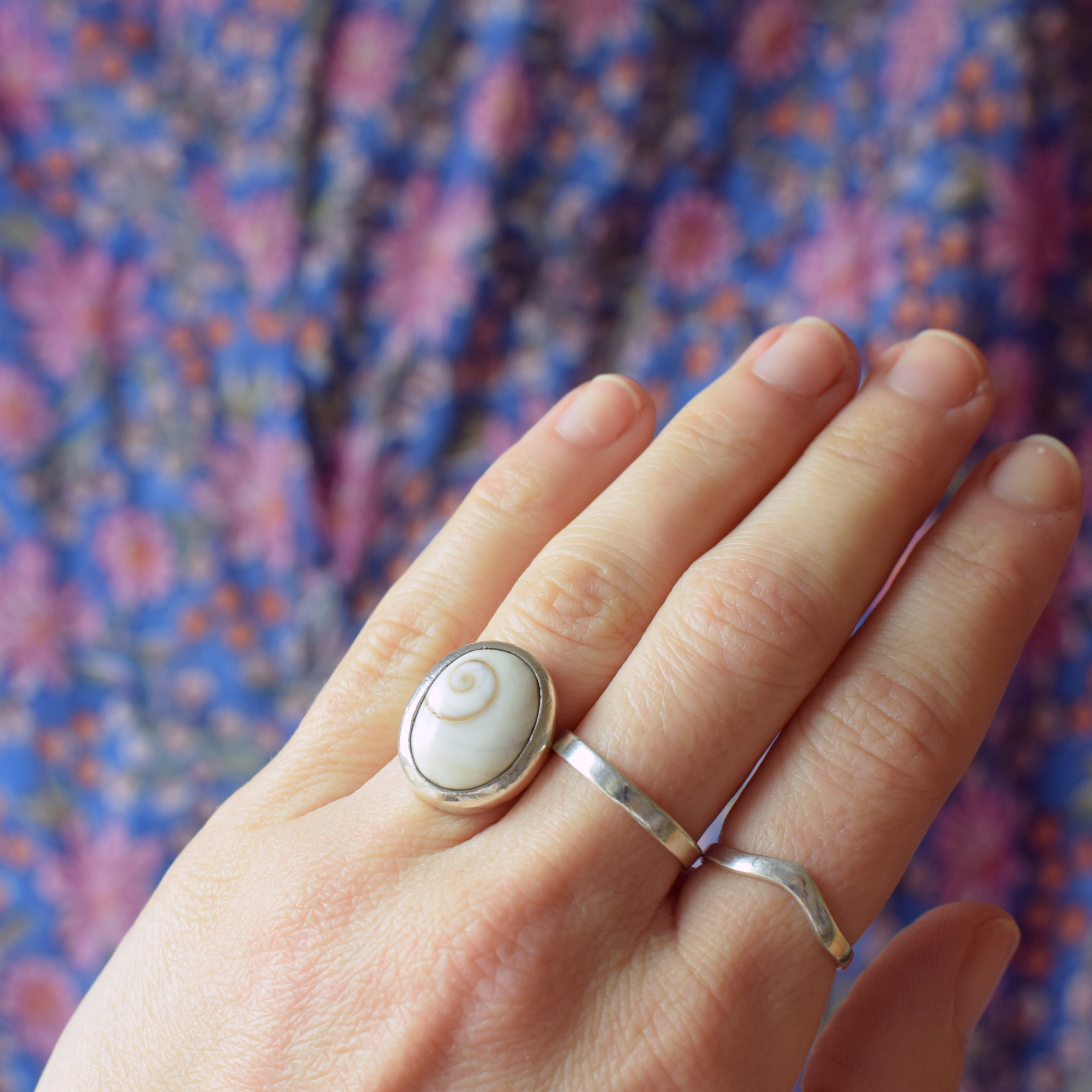 Hand wearing two silver rings with a floral pattern in the background