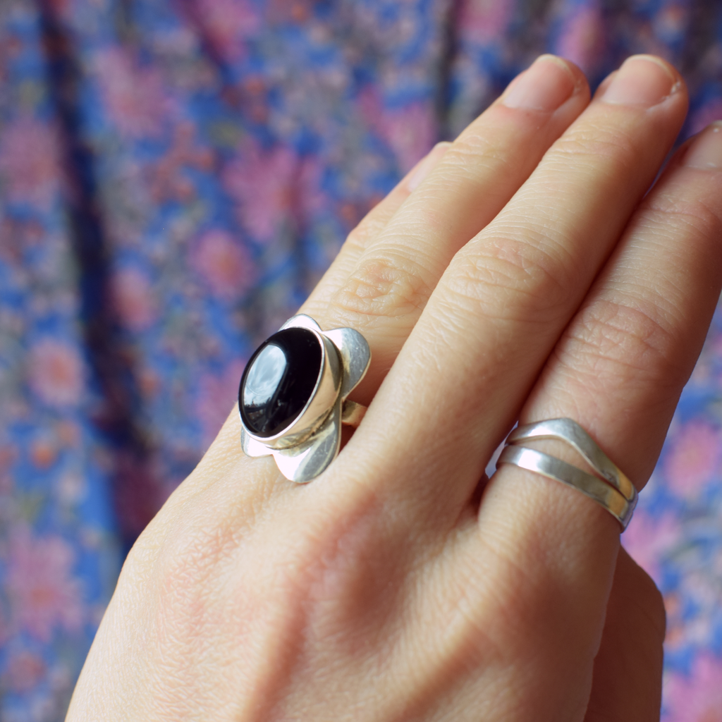 Hand wearing two silver rings with a black stone against a floral background