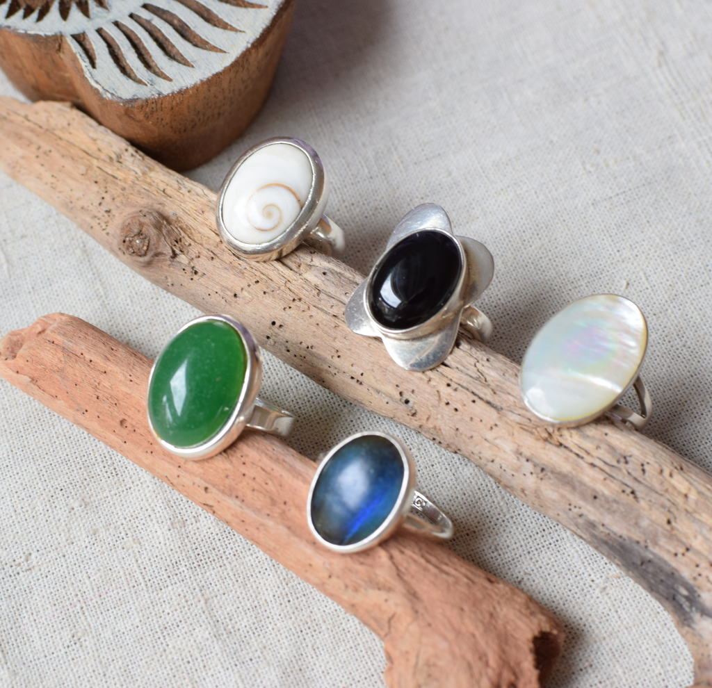 Five silver rings with different colored stones on a wooden surface