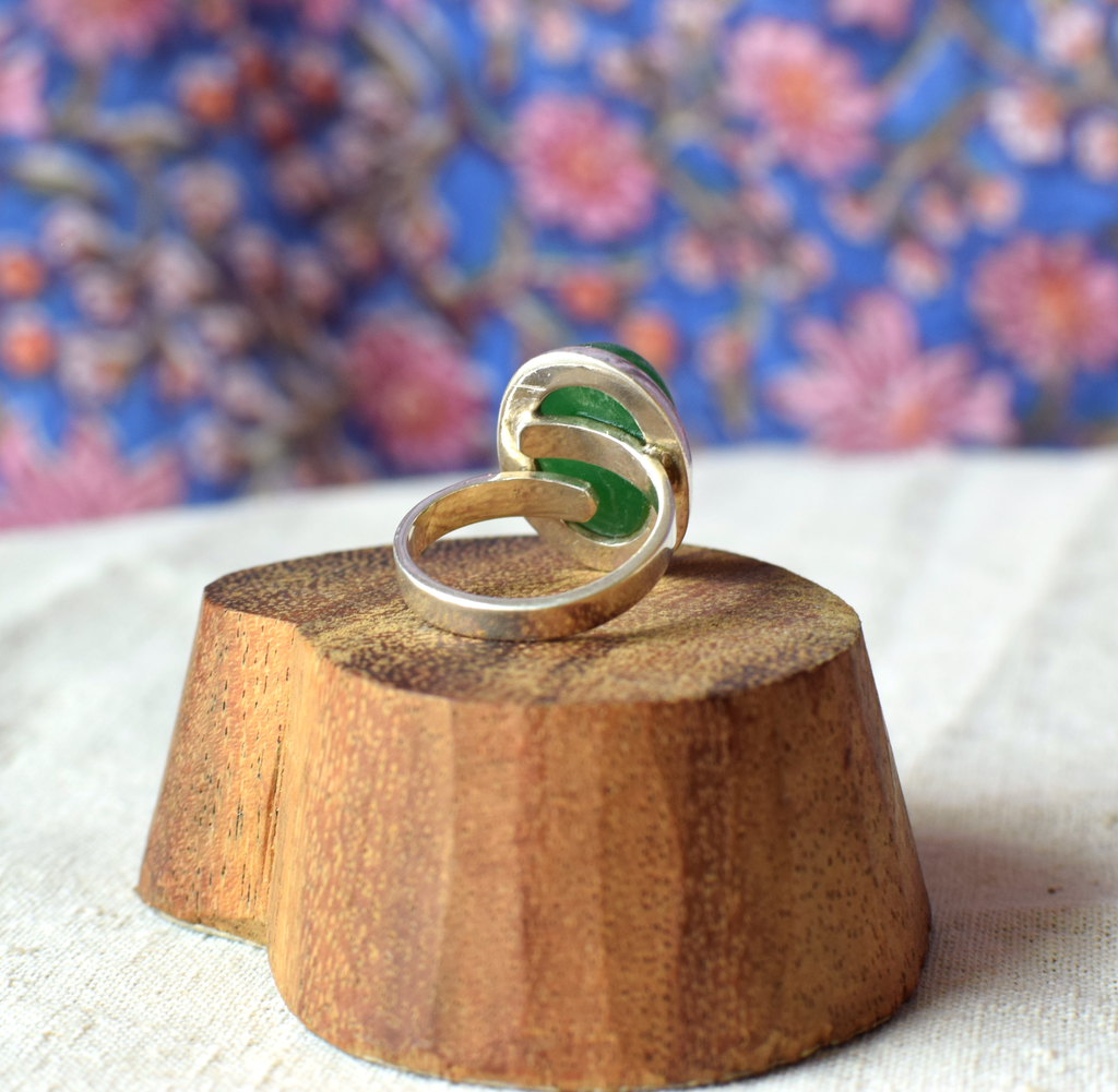 Silver ring with green stone on a wooden block against a floral background