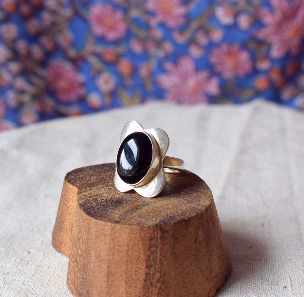 Silver ring with a black stone on a wooden stand against a floral background