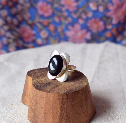 Silver ring with a black stone on a wooden stand against a floral background